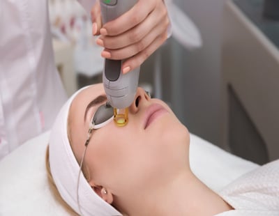 Therapist beautician makes a laser treatment to young woman's face at beauty SPA clinic. Facial laser hair removal epilation procedures. Face care rejuvenation medical correction for model by apparatus in salon. Close up, selective focus.