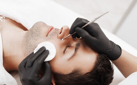 Cosmetician using blackhead remover for cleaning man face in spa salon