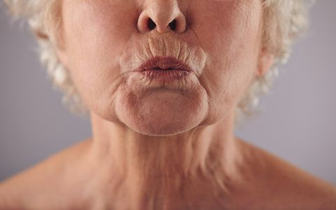 Close-up portrait of mature woman puckering lips against grey background. Senior woman grimacing. Focus on lips.