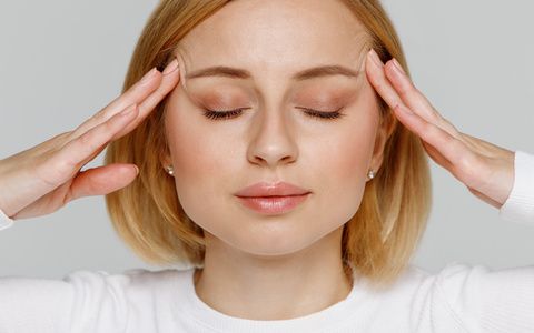 Woman meditating and massaging her temples, closes eyes, relieves emotional stress and nervous tension, exhausted from overwork, isolated on grey background. Fatigued worker suffering from headache.