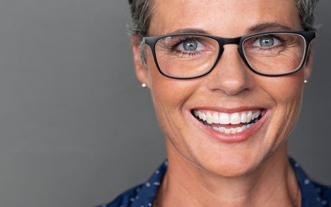 Portrait of happy mature woman wearing eyeglasses and looking at camera. Closeup face of smiling senior woman against grey wall wearing spectacles. Successful businesswoman feeling happy wearing glasses on gray background with copy space.