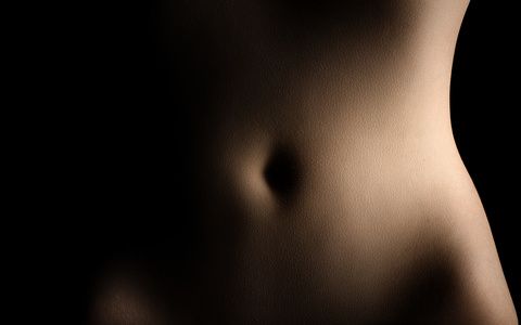 Low key bodyscape image of a woman's abdomen and hips against a black background