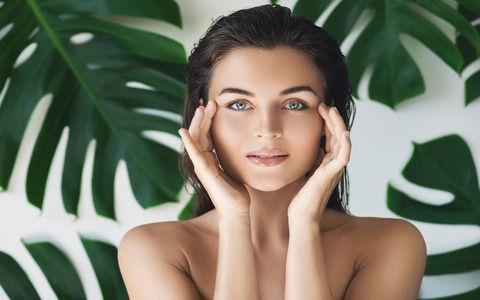 Portrait of young and beautiful woman with perfect smooth skin in tropical leaves. Concept of natural cosmetics and skincare.